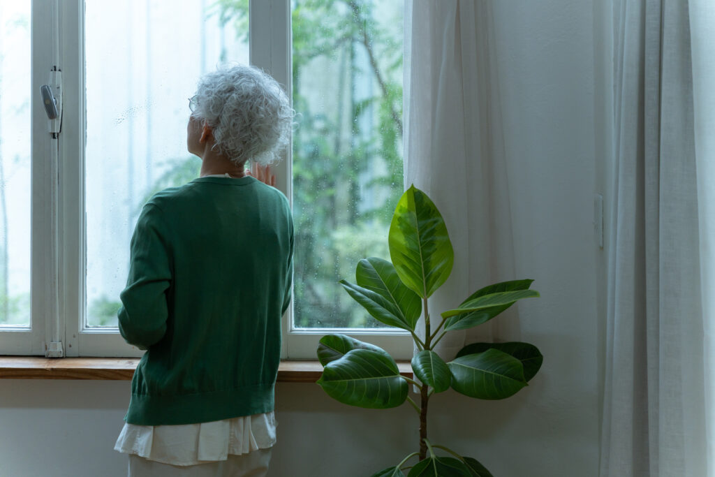 窓の外の雨を眺める老女性